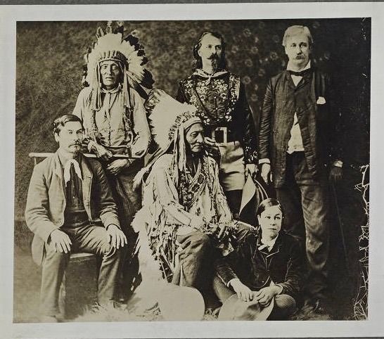 Standing in back row (from left) Crow Eagle; William Frederick "Buffalo Bill" Cody; and Adirondack, a naturalist. Seated in front, (from left) is William Halsey, Sitting Bull's interpreter; Hunkpapa Sioux Chief Sitting Bull; and young Johnny Baker, later known as the "Cowboy Kid" in the Wild West Show and foster son to Cody. / Historic photo, Huntington Digital Library